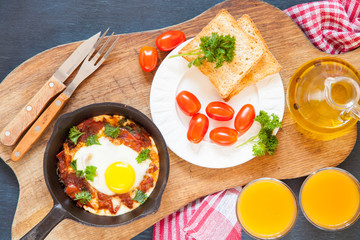 Pan of fried eggs and cherry-tomatoes with bread on dark table surface, top view, copy space, selective focus