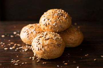 Four buns with seeds on a dark wooden background, top view