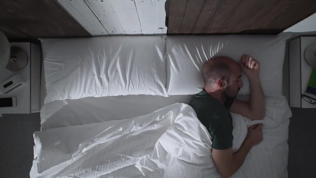 Young adult man with nightmares can't sleep at night. He turns in bed and wakes up suddenly.