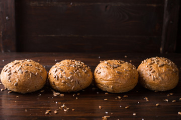 Four buns with seeds on a dark wooden background, top view