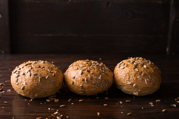 Four buns with seeds on a dark wooden background, top view