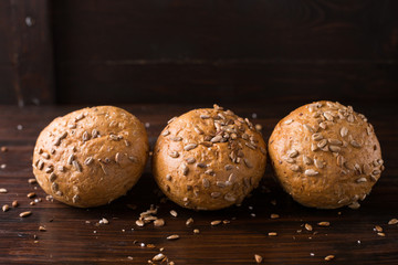 Four buns with seeds on a dark wooden background, top view