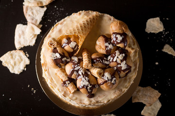Napoleon cake on a dark wooden background decorated with petals of almonds eclairs, waffles and chocolate icing