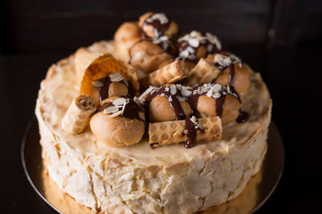 Napoleon cake on a dark wooden background decorated with petals of almonds eclairs, waffles and chocolate icing