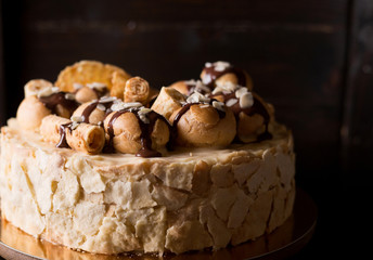 Napoleon cake on a dark wooden background decorated with petals of almonds eclairs, waffles and chocolate icing