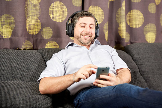 Man with headphones and phone smiling on sofa