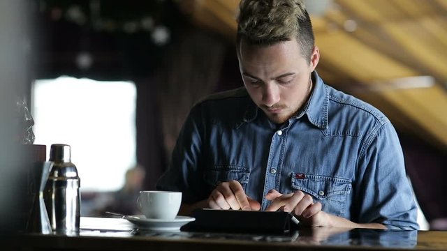 Young man typing on a tablet while sitting at the bar