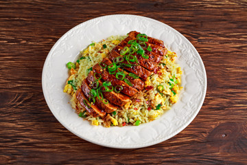 Chinese style Egg fried rice with sliced pork fillet on wooden table.