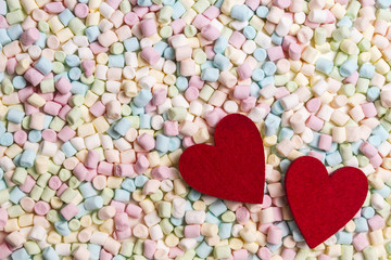 Two red hearts on colorful mini marshmallows background