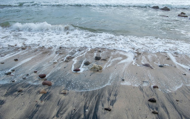 Moving wave hit the beach, touching the black and yellow sand. Showing white foam.  Captured on Menganti Beach, Kebumen, Indonesia