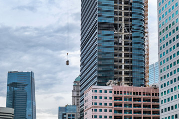 Photo of skyscrapper building under construction, when the builder lifting construction material into the top using crane. Captured in Jakarta, Indonesia