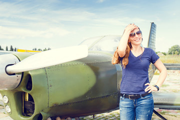 Young happy woman standing near sport plane on airfield delighted before flight.