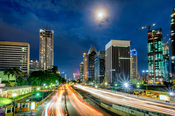 Iconic skyline and light trail of heavy traffic in Sudirman Street, Jakarta, Indonesia at dusk, showing light trail  of busy traffic and iconic skyscrapers in Jakarta, iluminated by moon light
