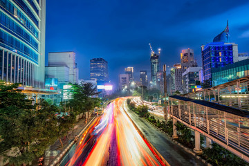Fototapeta premium Iconic skyline and heavy traffic in Sudirman Street, Jakarta, Indonesia at dusk, showing light trail of busy traffic and iconic skyscrapers in Jakarta. Urban Skyline, Building Exterior, Capital