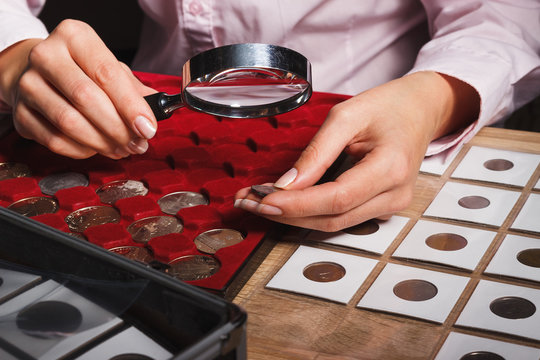Woman looks at the coin through a magnifying glass