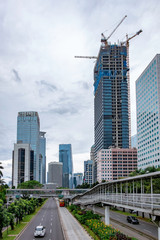 Photo of skyscrapper building under construction, with scenery of empty traffic and other skyscraper buildings. Captured in Jakarta, Indonesia