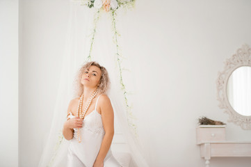 Curly blonde girl in a white silk gown boudoir robe on bed.