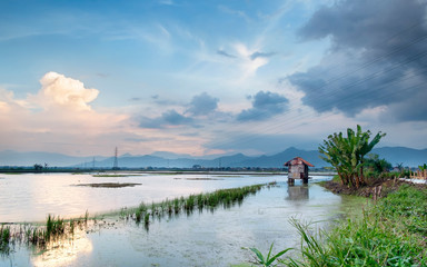 Photo of small hut in the middle of large pond, with beautiful sky and mountain in the background, captured at sunset, in Bandung, Indonesia.