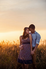 Loving couple stands in the middle of the wheat field at sunrise