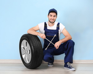 Young mechanic in uniform with spanner and wheel, on blue background