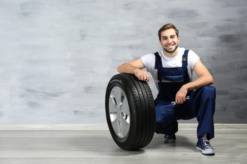 Young mechanic in uniform with spanners and wheel on gray background