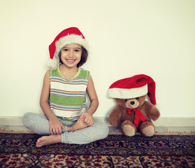 Little kid in Santa hat with cute teddy bear waiting at home for