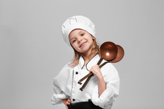 Cute girl in chef uniform on light background