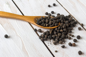 Closeup view of black pepper corns and spoon on white wooden background