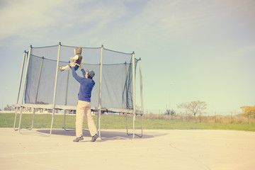 Back view of parent with child and trampoline. Family time on outdoors background