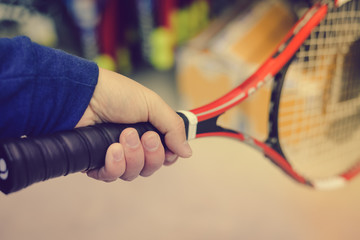 Closeup on person holding tennis racket in his hand on shopping mall background