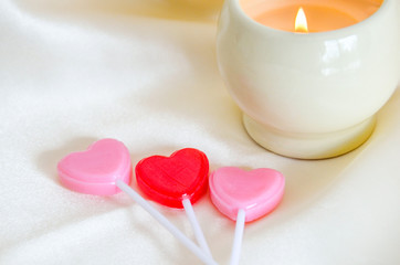 Red and pink hearts on silk cloth with a lit candle in the background.  Valentine's day, wedding, anniversary, romantic symbol of love.  Relaxing spa setting.