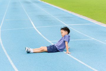 Young Asian boy sit on blue track in the stadium