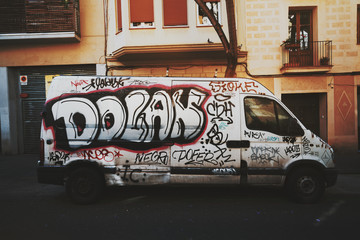 Abandoned car slovenly painted with graffiti parked on the street of european city with residential house behind it