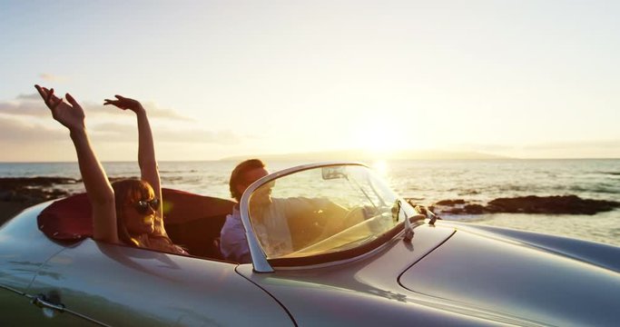 Happy Couple Driving into Sunset in Classic Vintage Sports Car by the Ocean. Romantic Sunset Drive. Shot on RED