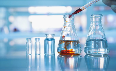 flask and vial with orange chemical drop by scientist hand
