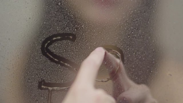 Girl writing SOS on glass in bathroom.