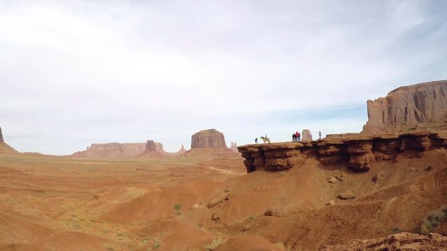 Zooming timelapse view on people at John Wayne point or cliff, between red sand and mountains at a orange desert, in monument valley, in Arizona and Utah border, United states of America