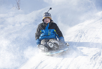 Fototapeta na wymiar Happy and excited boy Sledding downhill on a snowy day