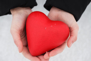 Red heart in female hands on a background of snow, top view