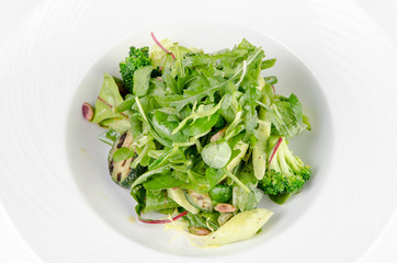 Salad of green vegetables with broccoli, zucchini and walnut dressing on a plate on a white background, closeup