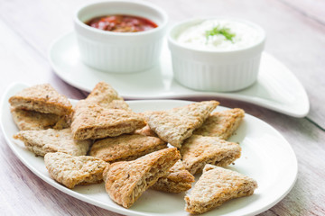 Crisps made of whole wheat pita bread. Two dips in the background: tomato sauce and cream cheese.