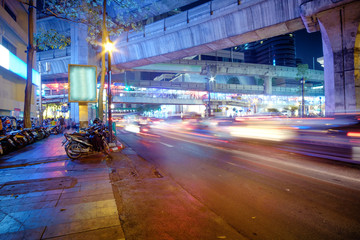 Night traffic lights of Bangkok highway with subway MRT line above the road and many scooters parked near the city center. Cityscape of the capital city of Thailand - Bangkok, Asia