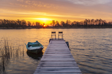 Fototapeta premium boat moored to a wooden bridge, a beautiful sunrise over the lak