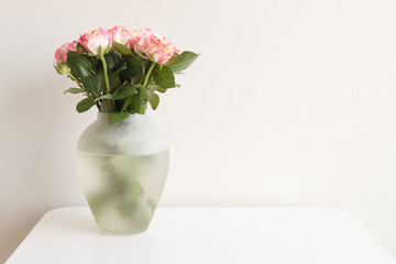 Pink and cream roses in glass vase on white table