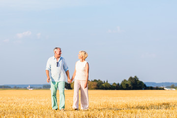 Senior Frau und Mann halten Hände beim Spaziergang über ein Feld