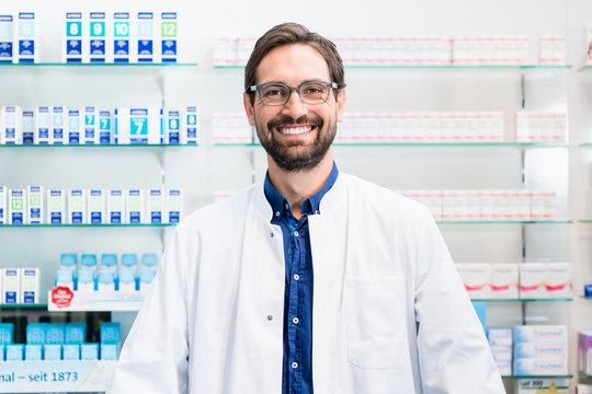 Apotheker in Apotheke steht vor Regal mit Medikamenten