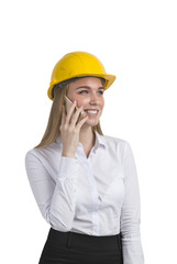 Isolated portrait of a businesswoman wearing a yellow hard hat and a white blouse and talking on her smartphone