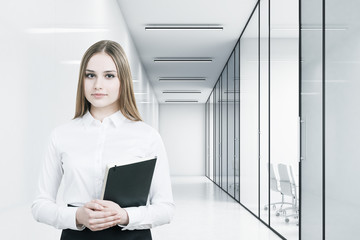 Young girl in an office suit is holding a black folder and standing in a white office corridor with conference rooms. 3d rendering. Mock up