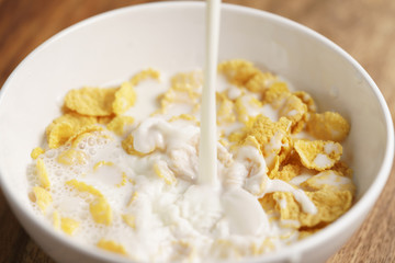 milk pour into bowl with corn flakes, preparing breakfast