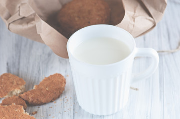 Fototapeta na wymiar Mug with milk and oatmeal cookies wrapped in paper edge